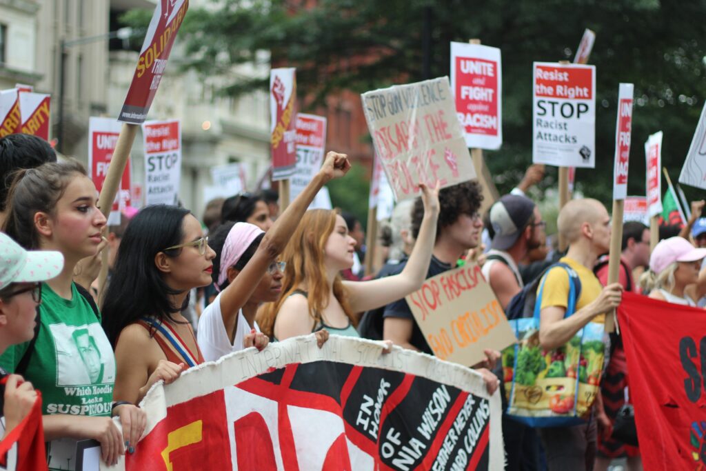 Group of people holding signage and raising their hands during daytime.
